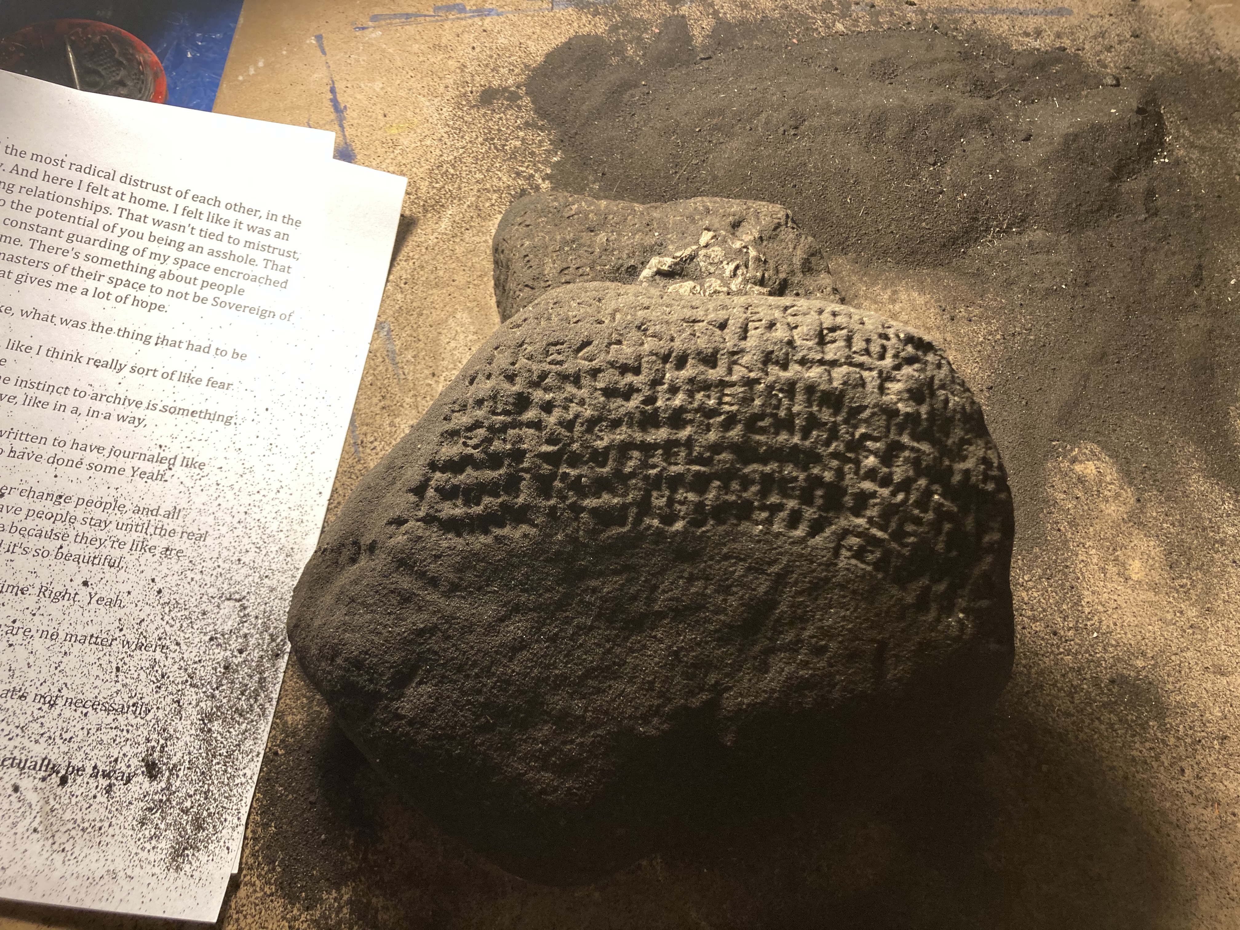 Sheets of paper with transcriptions of the recordings next to a piece of asphalt where text has been carved on half of it.