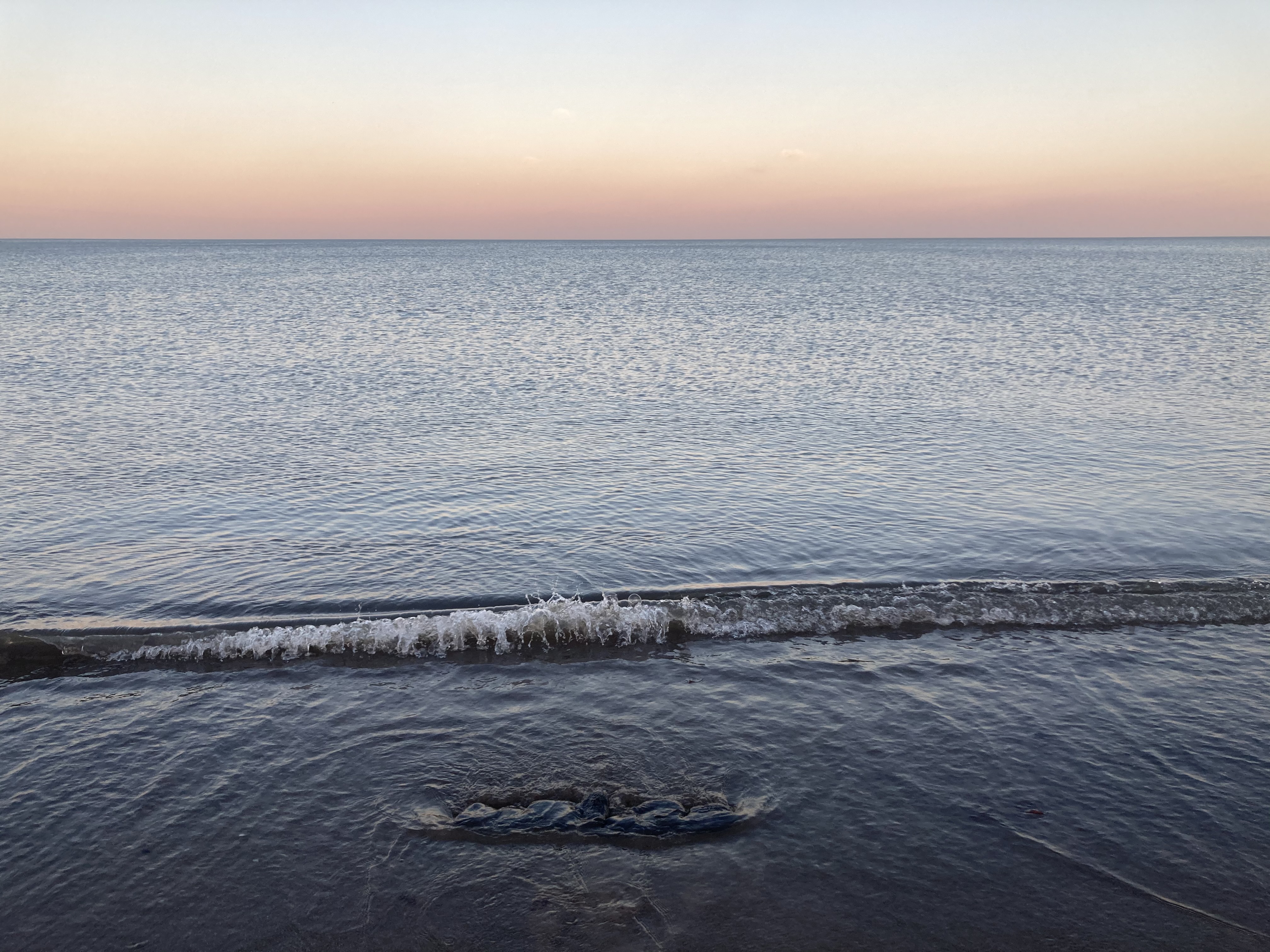 Four images of tides washing over a line of asphalt rocks.